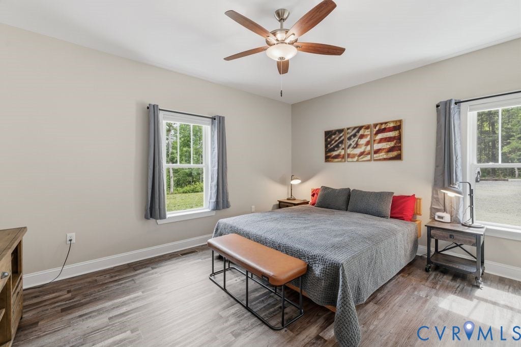 3259 Three Bridge Road, Powhatan, VA 23139 Spacious room featuring wood-finish flooring, two large windows with white trim, a ceiling fan with integrated lighting, and neutral wall tones