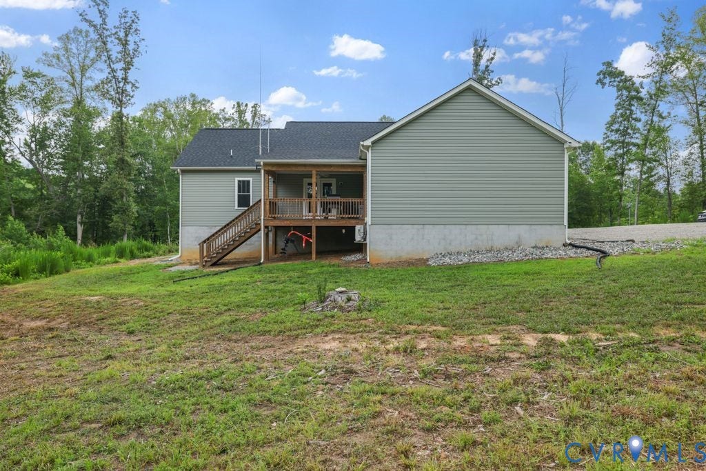 3259 Three Bridge Road, Powhatan, VA 23139 Rear exterior featuring light green siding, a covered wood deck, wood stairs, a black shingle roof, and a gravel perimeter