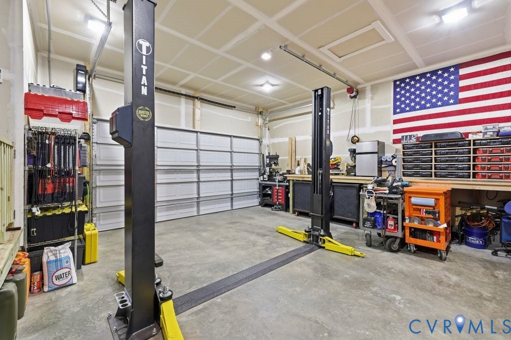 3259 Three Bridge Road, Powhatan, VA 23139 Spacious garage featuring a two-post vehicle lift, dual overhead garage doors, workbench with shelving, and recessed ceiling lighting