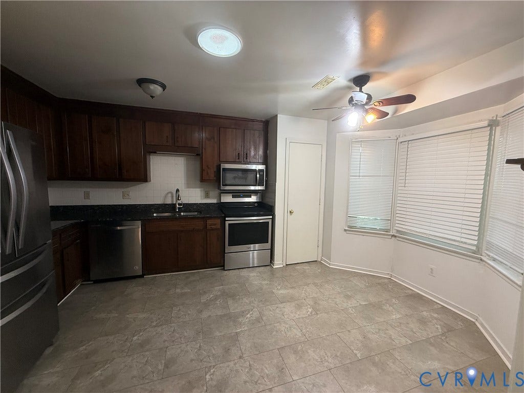 Kitchen featuring dark wood cabinetry, stainless steel appliances, a bay window, and tile flooring