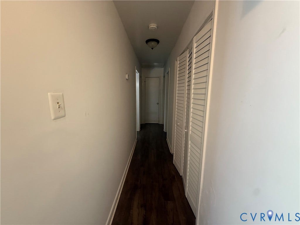Hallway featuring wood-finish flooring, light-toned walls, louvered bi-fold doors, and a ceiling-mounted light fixture