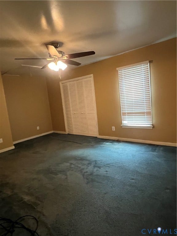 Spacious room with dark carpet flooring, neutral-toned walls, and a ceiling fan with integrated lighting