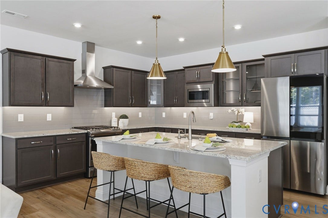 10880 Farmstead Mill Lane, Glen Allen, VA 23059 Spacious kitchen featuring dark wood cabinetry, stainless steel appliances, a large island with a light-toned countertop, a tile backsplash, and recessed and pendant lighting