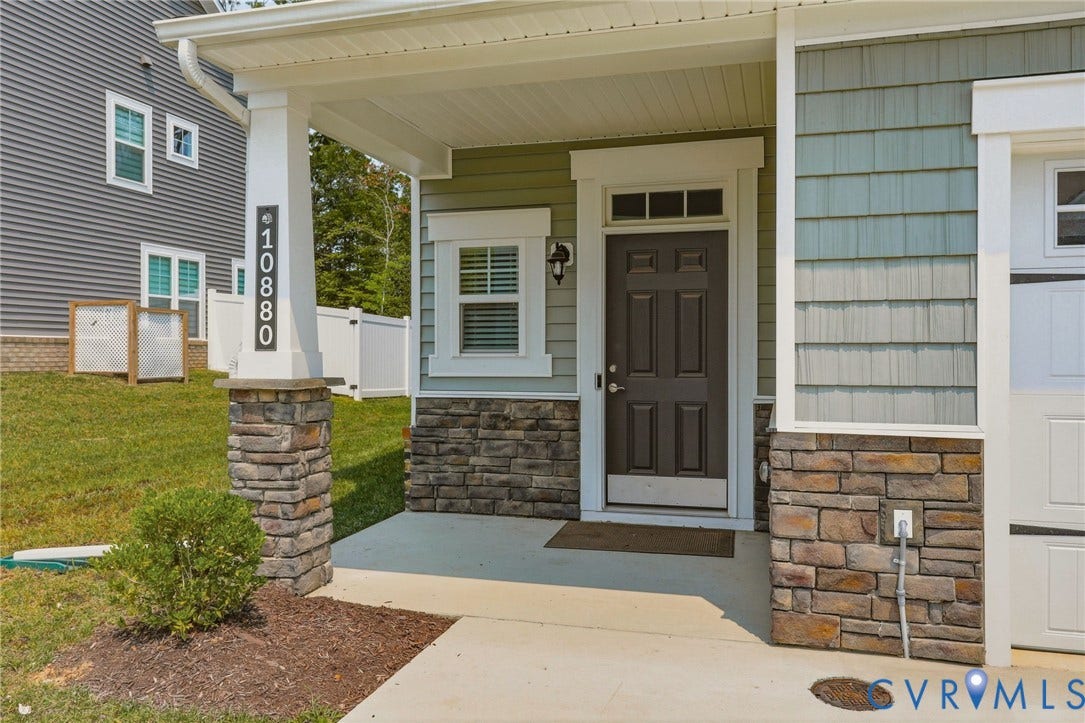 10880 Farmstead Mill Lane, Glen Allen, VA 23059 Covered front porch featuring stacked stone accents, vinyl shake siding, and a dark paneled entry door with transom window