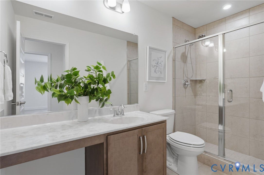 10880 Farmstead Mill Lane, Glen Allen, VA 23059 Bathroom featuring a wood-finish vanity with an integrated sink, a large mirror, and a tiled shower with a glass enclosure