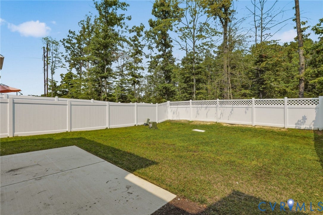 10880 Farmstead Mill Lane, Glen Allen, VA 23059 Expansive grassy yard featuring a concrete patio, full white vinyl fencing with lattice accents, and mature perimeter trees