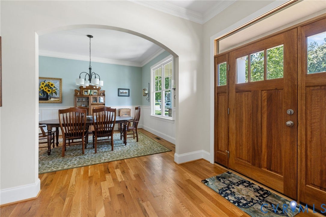 15936 Alsdell Road, Hallsley, Midlothian, VA 23112 Warm wood-finish flooring extends from the entryway, featuring a craftsman-style door with multiple lites and a transom window, into an arched doorway leading to a dining area with wainscoting and a chandelier
