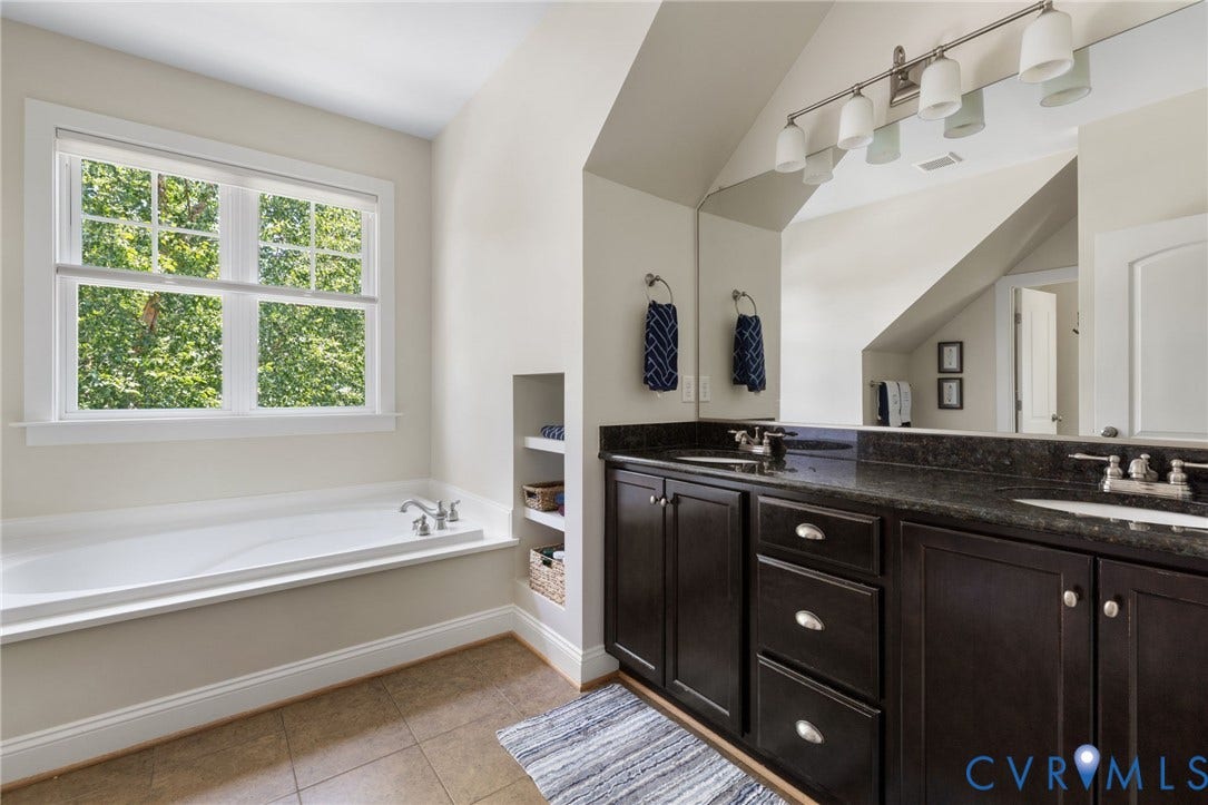 15936 Alsdell Road, Hallsley, Midlothian, VA 23112 Bathroom featuring a dual vanity with a dark countertop and undermount sinks, an integrated soaking tub, built-in shelving, and a large window with grid panes