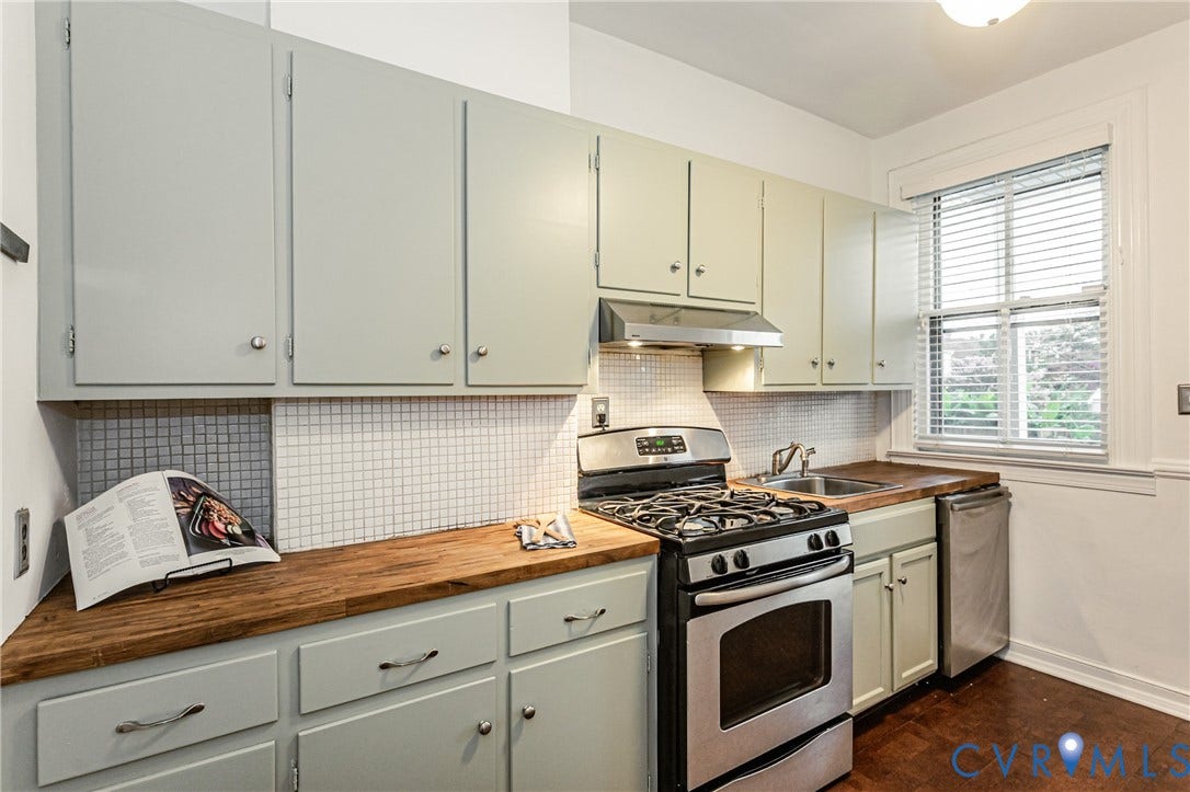 Kitchen featuring light-toned cabinetry, wood-finish countertops, and a white mosaic tile backsplash