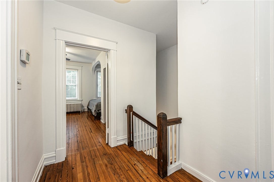 Hardwood flooring extending through the hallway and into a room with a double-hung window and baseboard heating