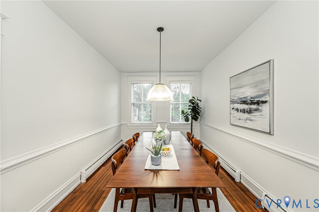 Dining area featuring wood flooring, white painted walls with chair rail and base molding, two double-hung windows, and a central pendant light fixture