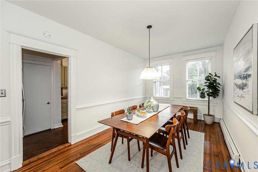 Dining area featuring hardwood flooring, crisp white walls with wainscoting, two windows, and a ceiling-mounted pendant light fixture