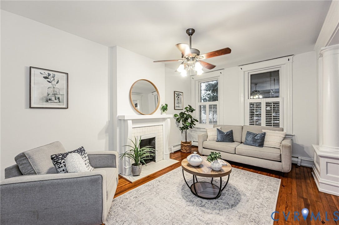 Living room featuring wood flooring, a white mantel, and a ceiling fan with light fixture