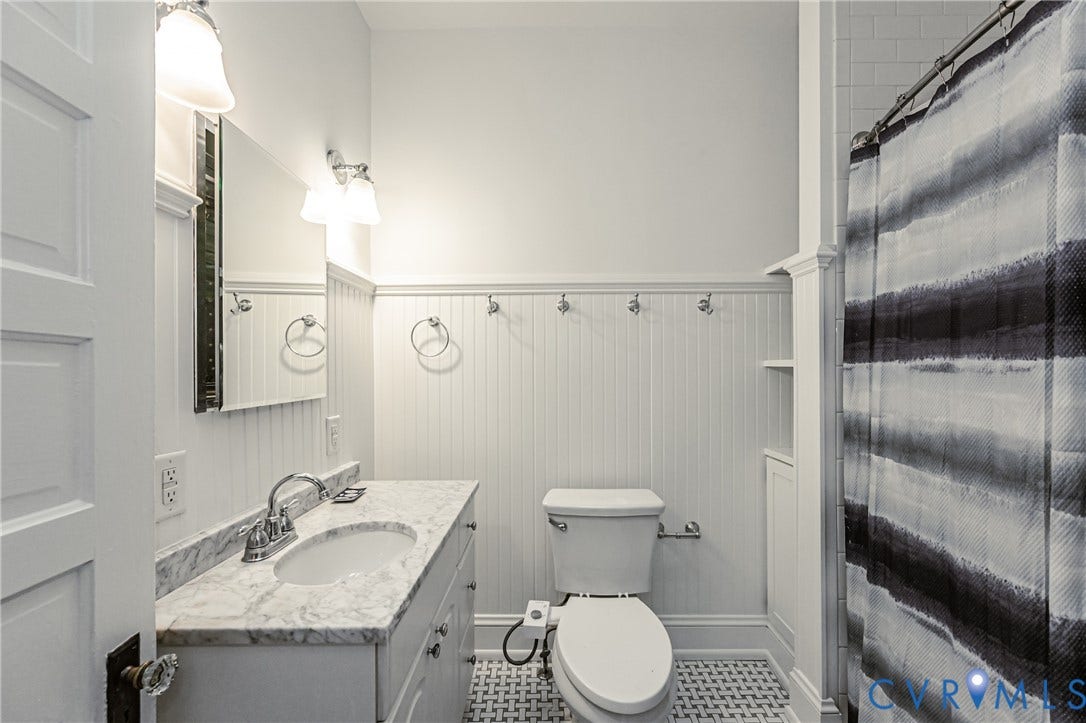 Bathroom featuring a white vanity with a marble countertop and undermount sink, beadboard wall paneling, mosaic tile flooring, and a built-in storage cabinet