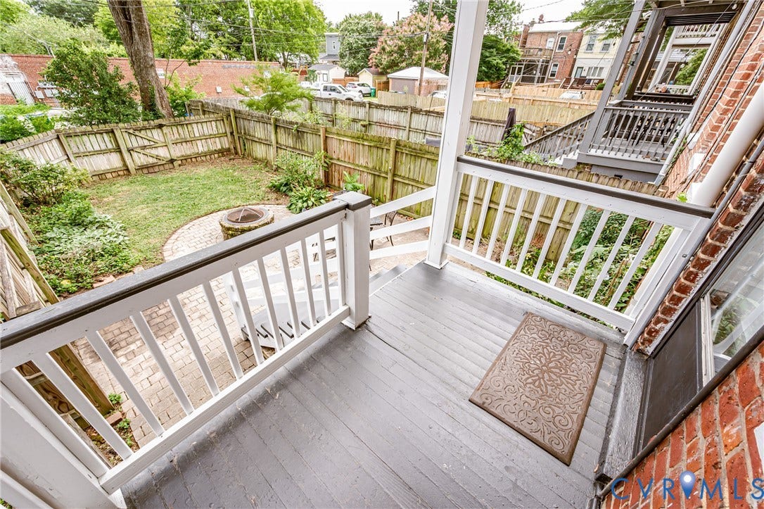 Rear balcony with dark wood-finish flooring, white railings, and brick exterior wall