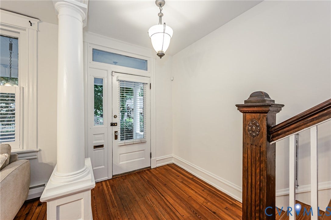 Inviting entryway featuring warm wood flooring, a classic white paneled door with transom window, and an elegant hanging light fixture