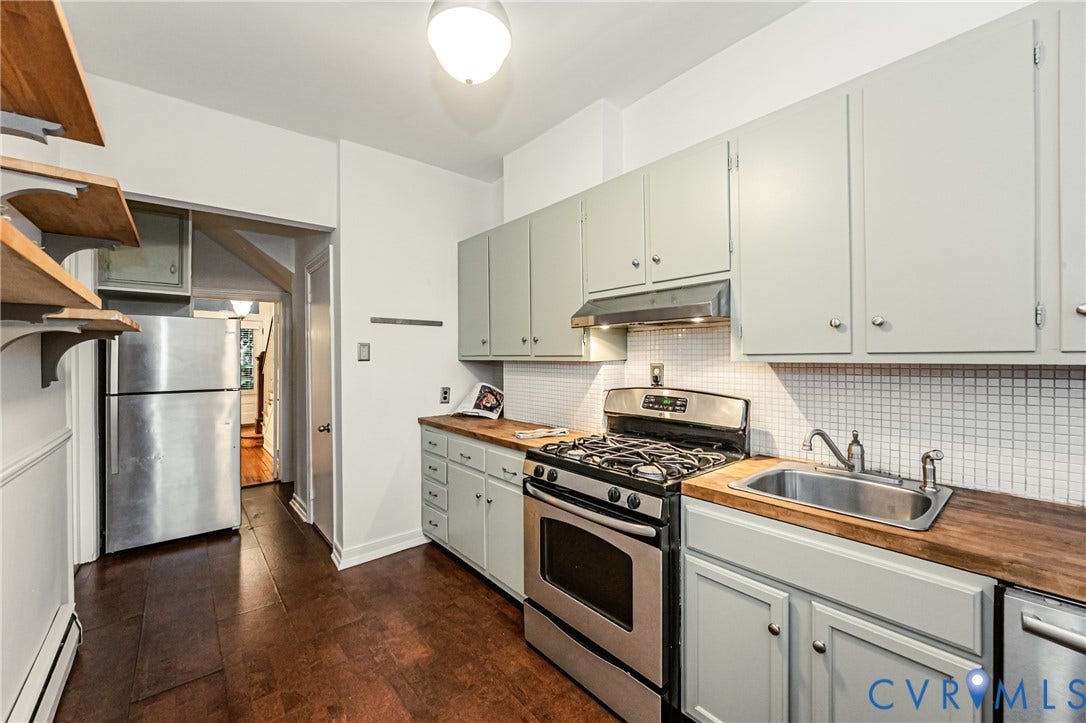 Kitchen featuring wood-finish flooring, light-toned cabinetry with metal hardware, butcher block countertops, white square tile backsplash, and stainless steel appliances