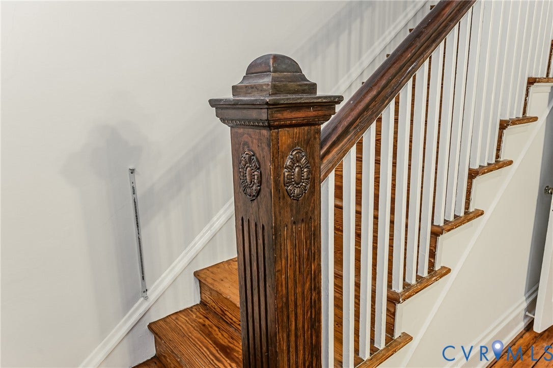 Staircase featuring a rich wood newel post with carved detailing, a coordinating wood-finish handrail, and white balusters