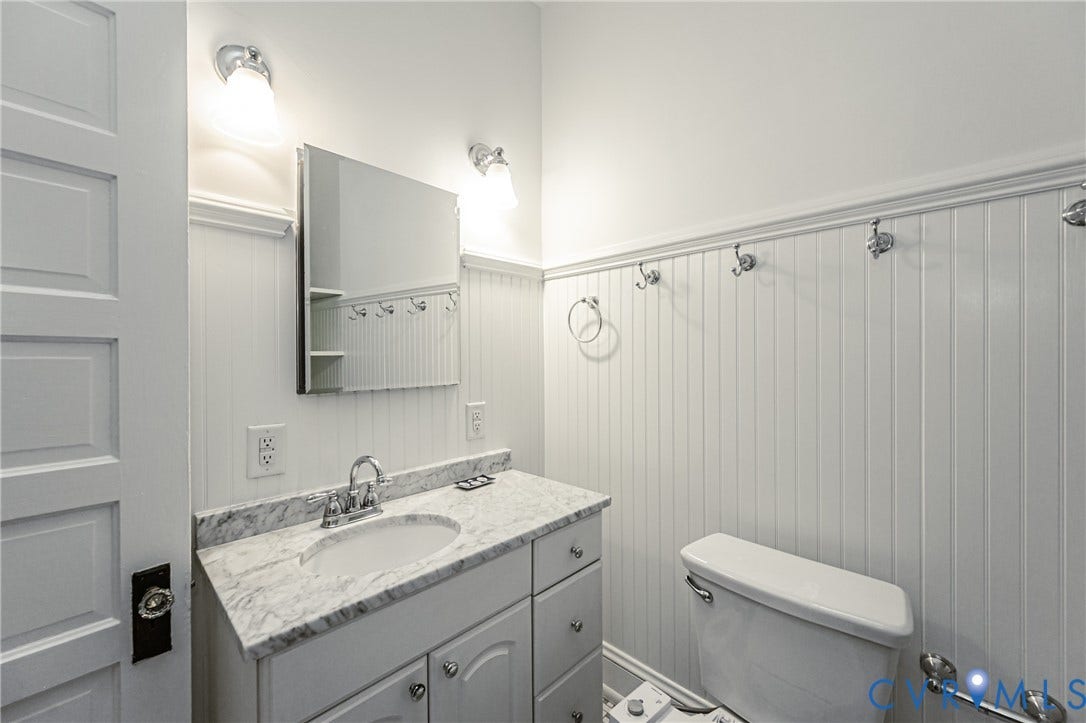 Bathroom featuring white beadboard paneling, a single vanity with a stone countertop and integrated sink, a chrome faucet, and a wall-mounted medicine cabinet with a mirrored front