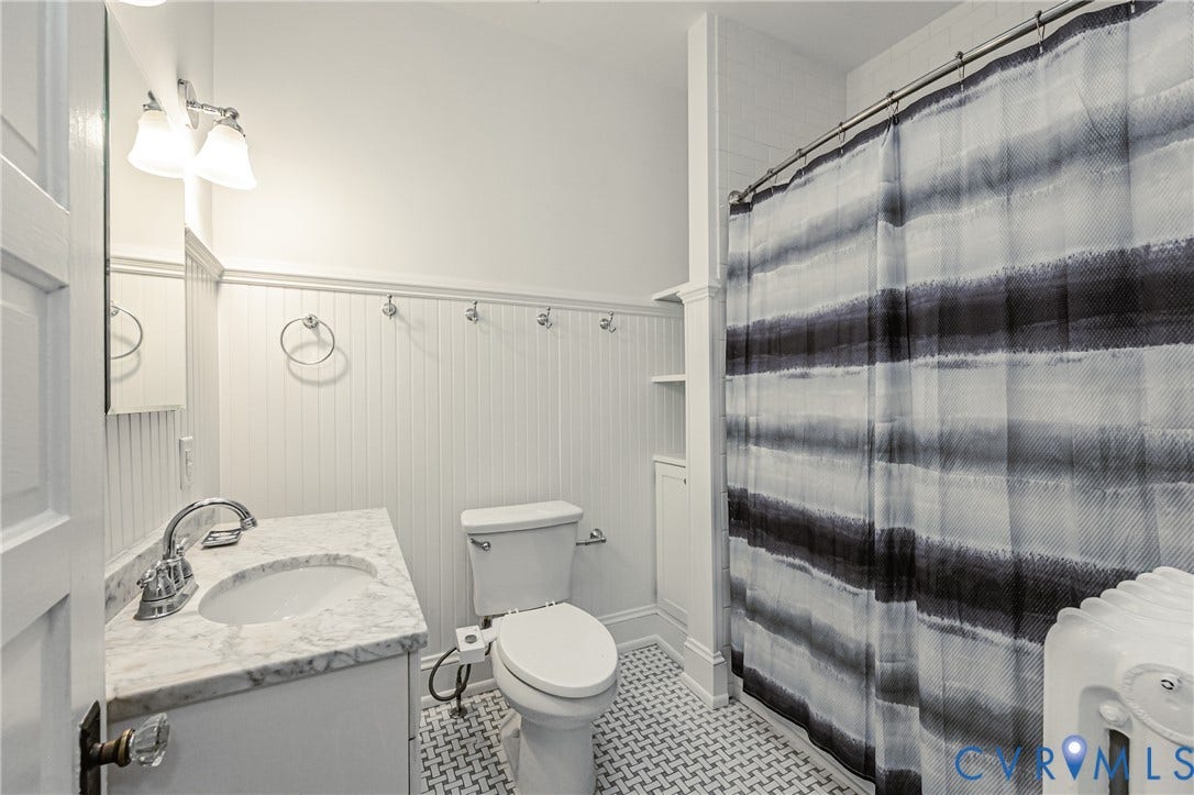 Bathroom featuring wainscoting, a vanity with a white marble countertop and integrated sink, chrome fixtures, and patterned floor tile