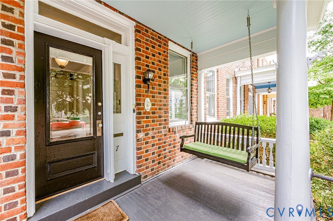 Brick facade home with a covered front porch, featuring a dark-paneled front door with sidelight, a traditional porch swing, and white column supports