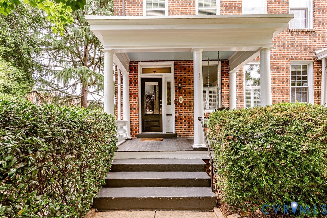Brick facade colonial featuring a covered front porch with white columns, dark wood entry door with transom window, and front steps with a wrought iron handrail