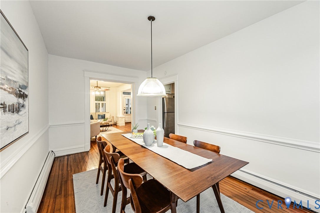 Dining space featuring wood-finish flooring, white walls with wainscoting, and an overhead pendant light