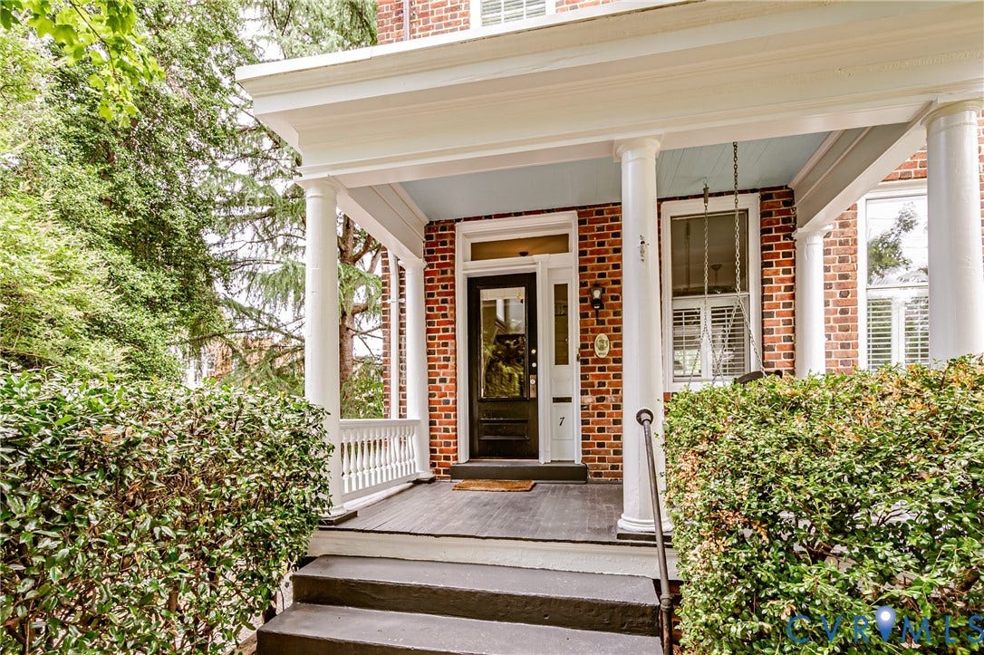 Brick facade residence featuring a covered porch with white columns, a painted light blue porch ceiling, and dark-stained wood flooring