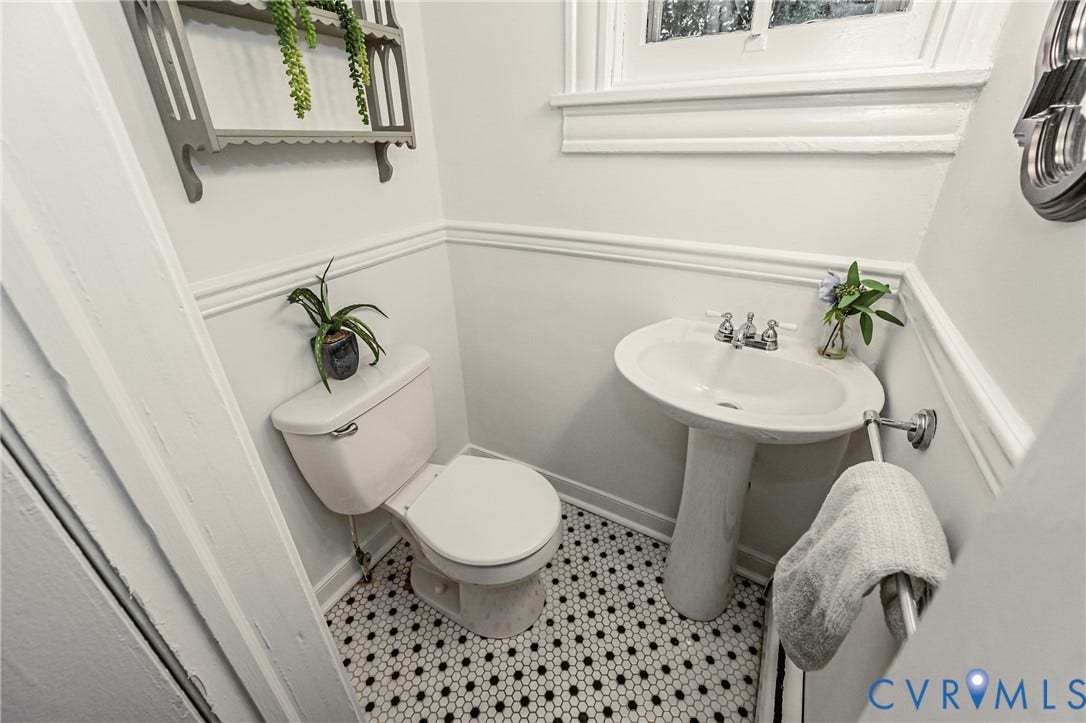 Pedestal sink with chrome fixtures, black and white hexagonal tile flooring, wainscoting, and a window for natural light