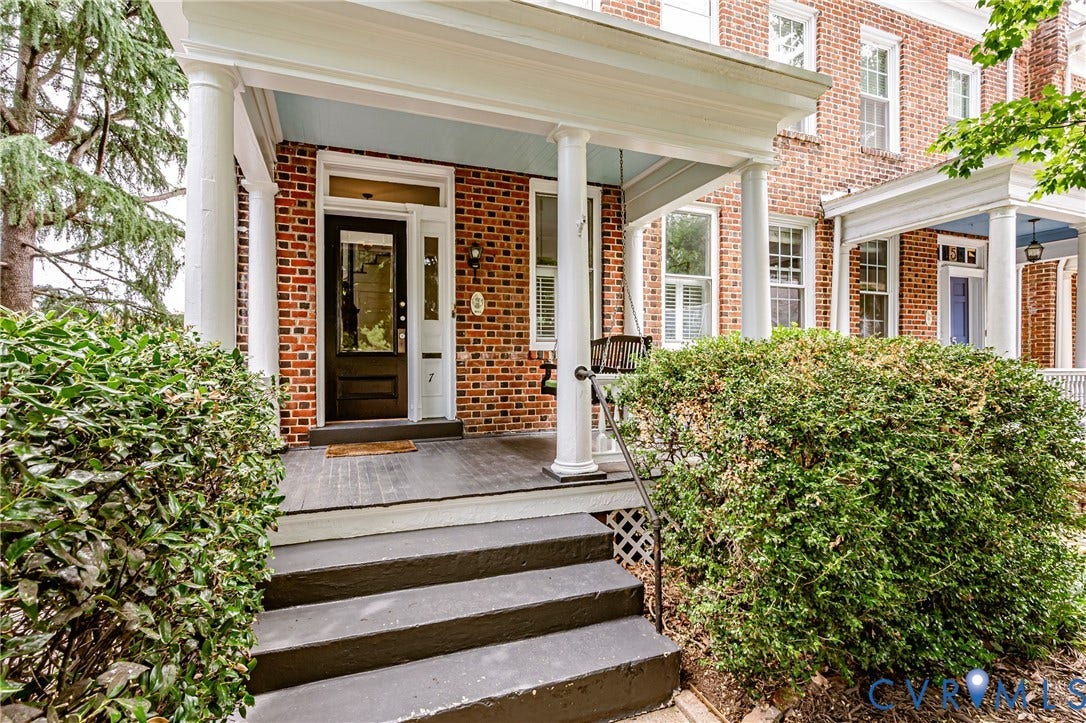 Brick facade residence featuring a covered front porch with white columns, dark wood-finish flooring, and a dark paneled entry door with transom window