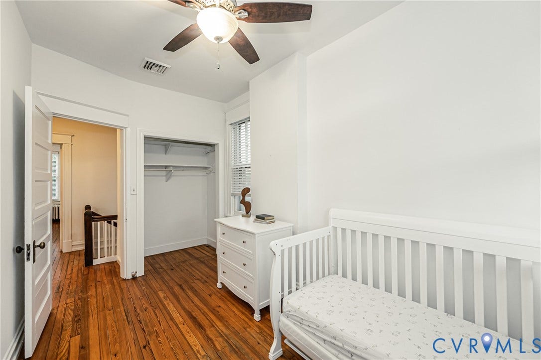 Hardwood flooring throughout, featuring a ceiling fan with integrated lighting, an open closet with shelving and hanging rod, a window with horizontal blinds, and a paneled interior door