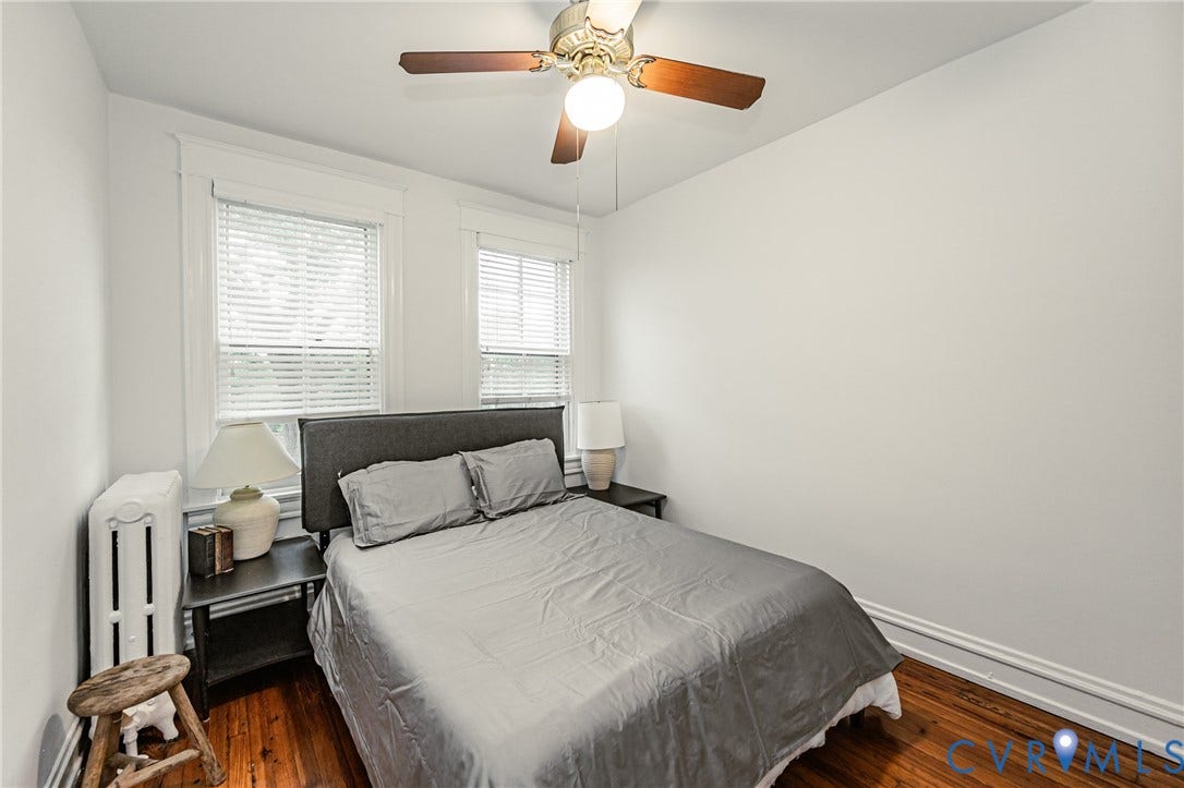 Room featuring wood flooring, two windows with blinds, and white trim