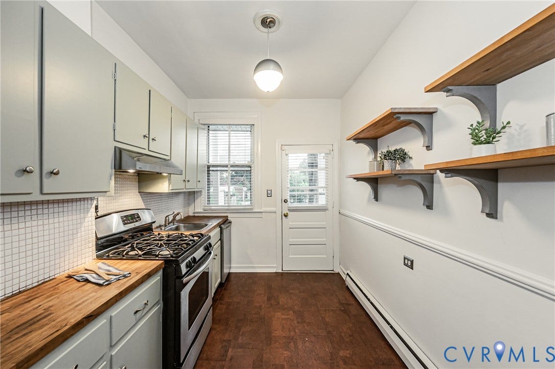 Galley kitchen featuring light-toned cabinetry, butcher block countertops, stainless steel gas range, and a tiled backsplash