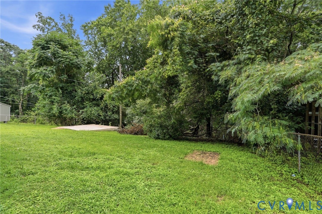 5301 Dalglish Road, Henrico, VA 23223 Expansive grass lawn featuring a concrete pad, mature trees, and a chain-link fence