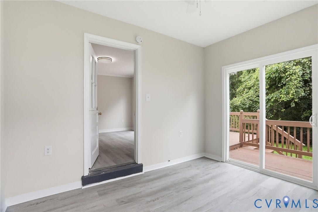5301 Dalglish Road, Henrico, VA 23223 Sliding glass door leading to a wooden deck, featuring light-toned flooring, white baseboards, and a doorway to an additional room