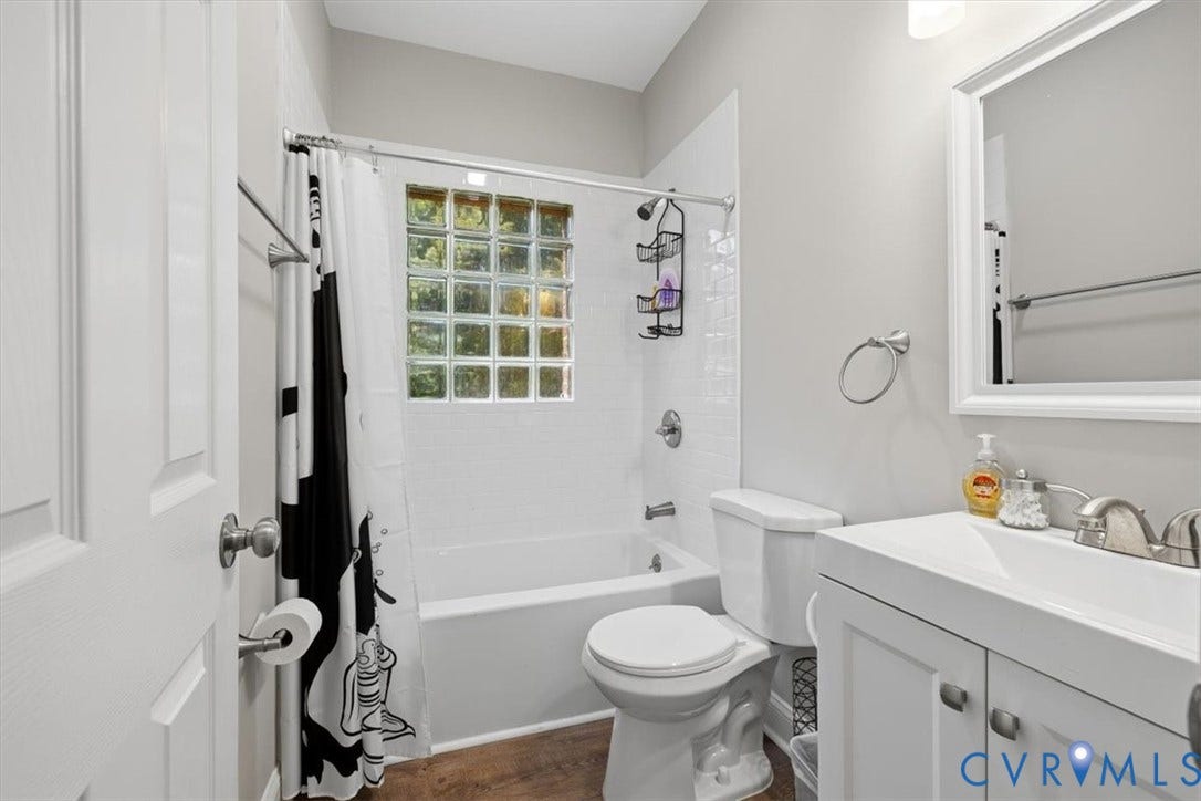 Full bathroom featuring a glass block window, white subway tile shower surround, a white vanity with integrated sink, and wood-finish flooring