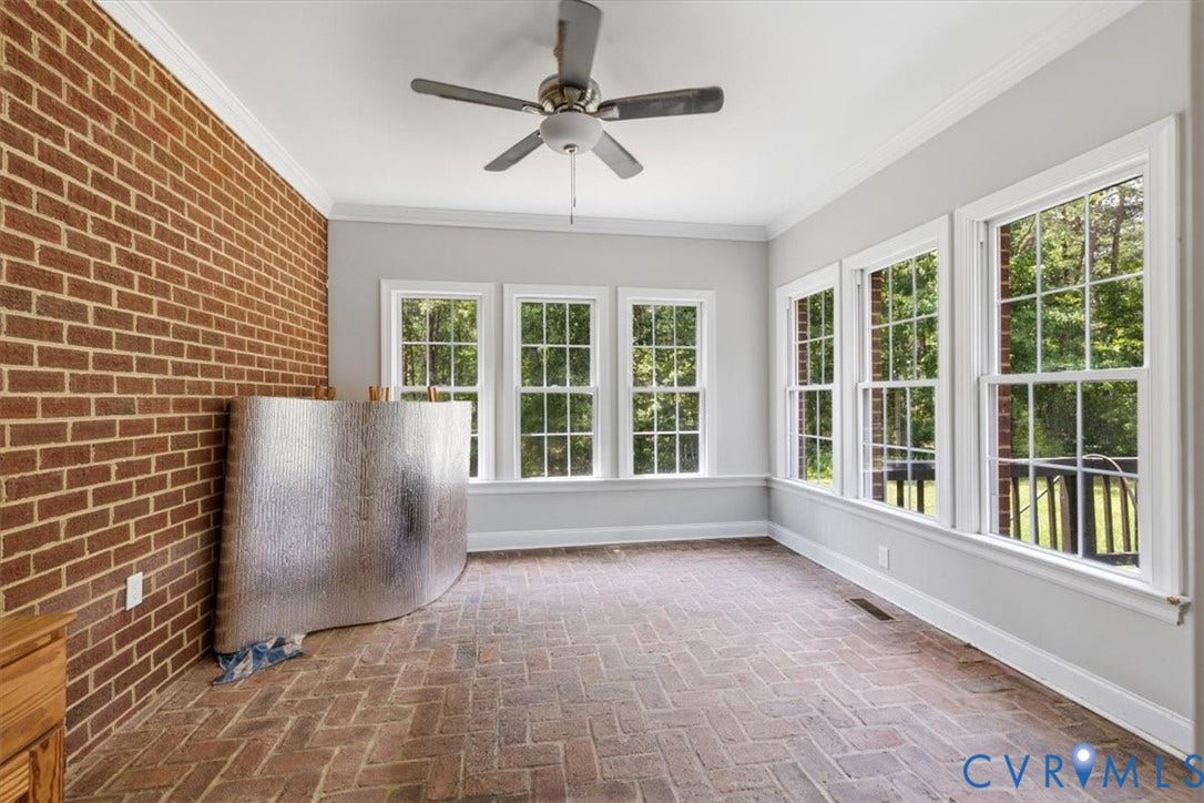 Sunroom featuring a brick accent wall, herringbone pattern brick flooring, multiple double-hung windows, crown molding, and a ceiling fan