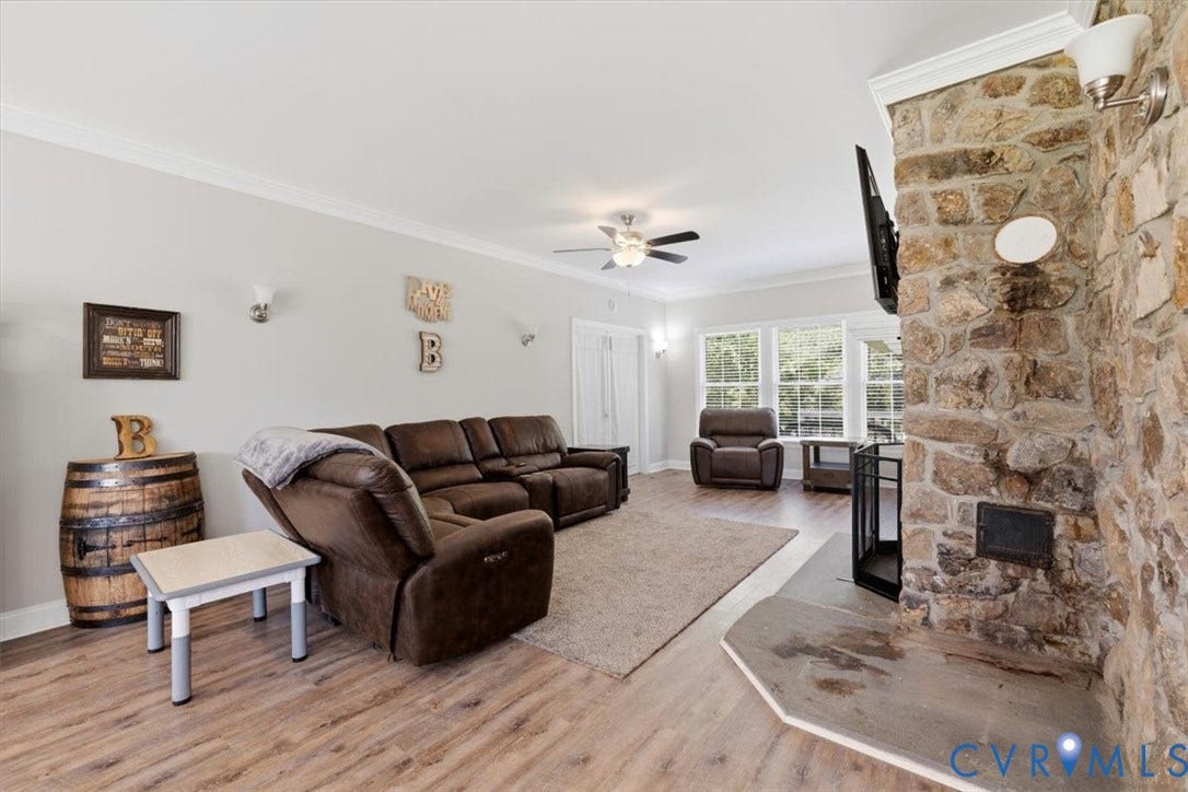Living area featuring a stone fireplace with hearth, wood-finish flooring, and crown molding