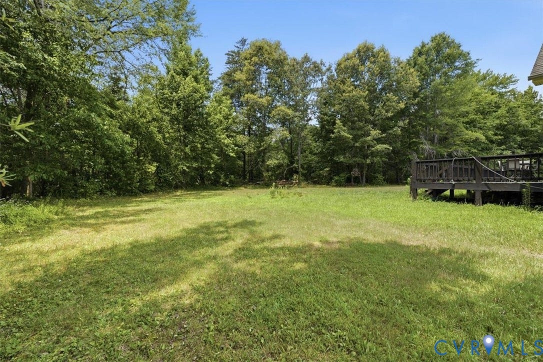 Expansive outdoor space featuring a large grassy area, mature trees, and a dark-stained wood deck