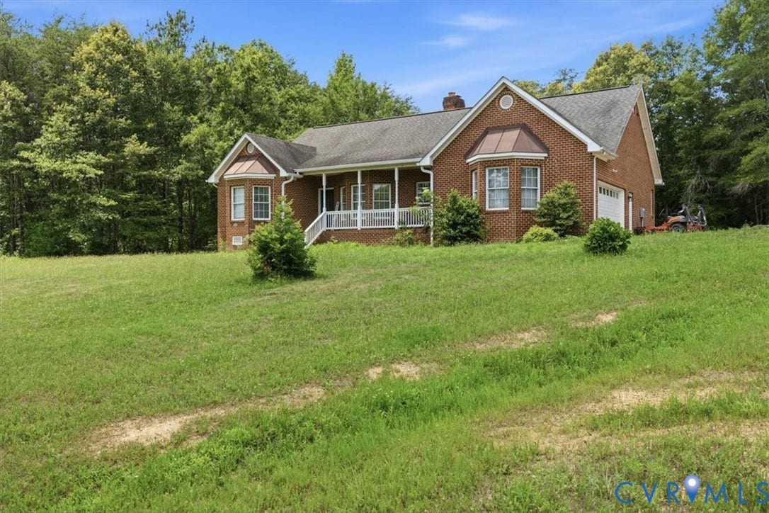 Brick exterior residence featuring a covered front porch with white railings, a bay window with a copper-tone awning, and an attached garage with a white door