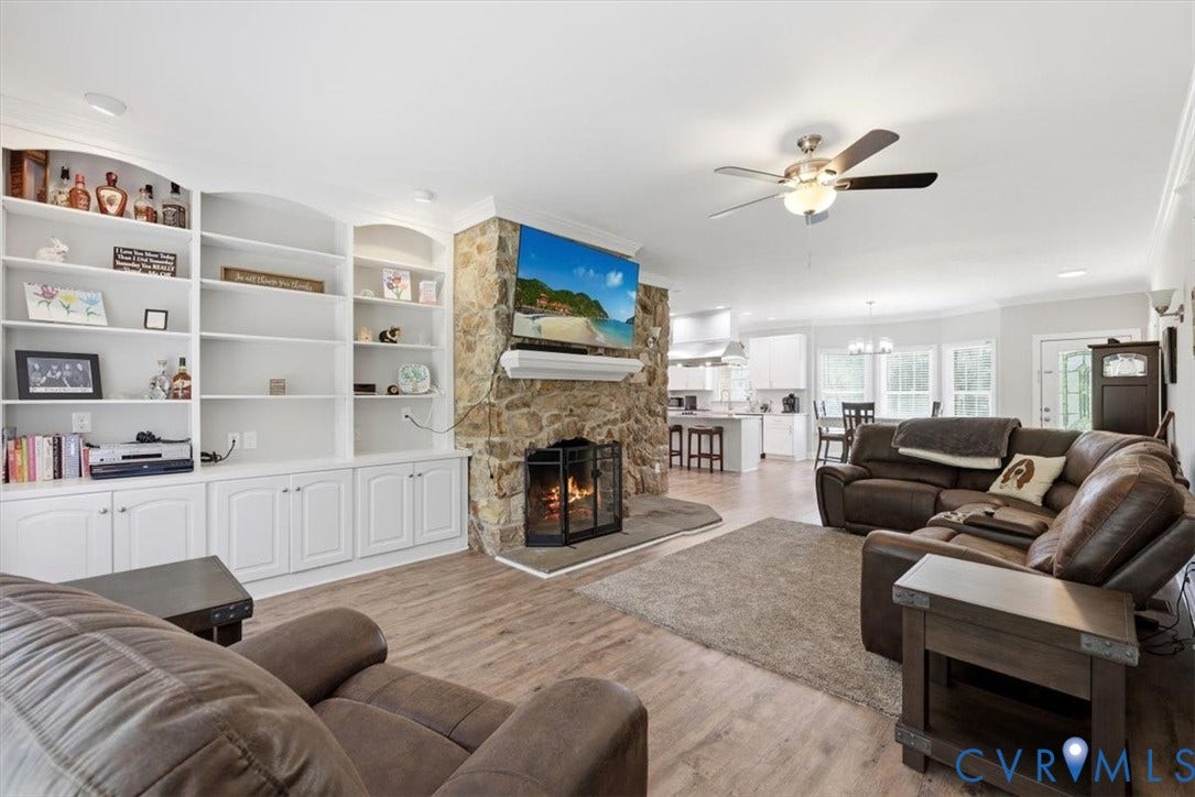 Spacious living area featuring a floor-to-ceiling stone fireplace, built-in shelving and cabinetry, recessed lighting, and wood-finish flooring