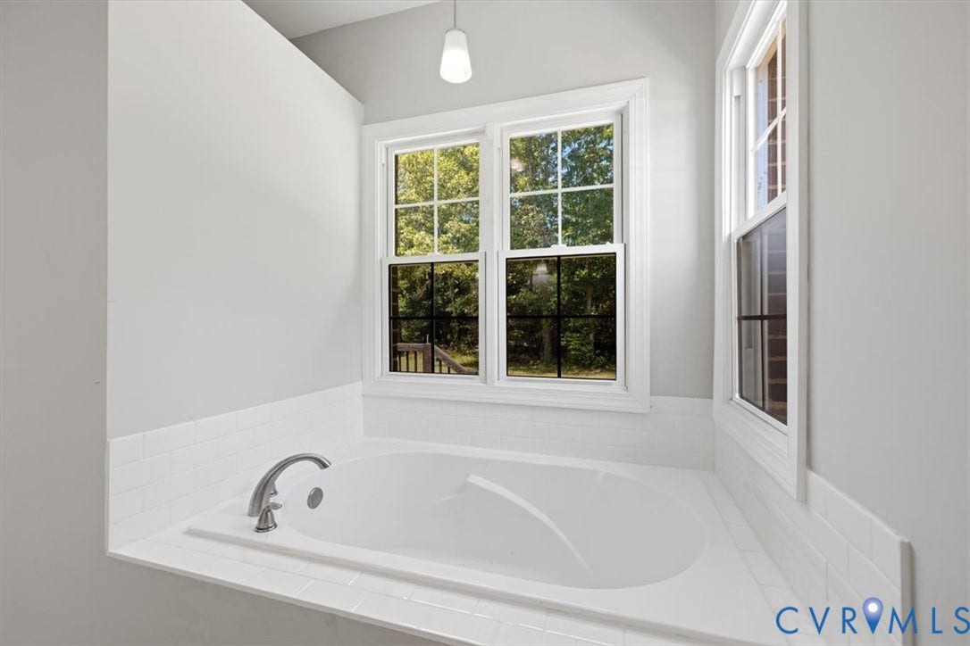 Freestanding soaking tub with brushed nickel fixtures and a surrounding white subway tile wainscoting