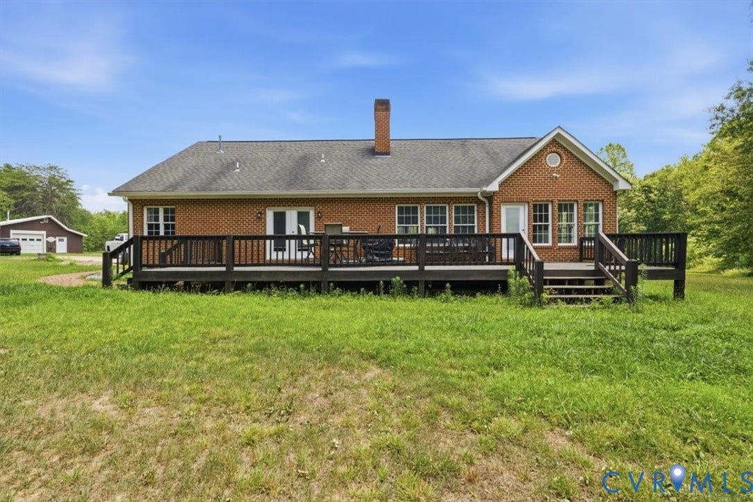 Brick exterior home featuring an expansive rear deck, multiple windows, double glass doors, and a detached outbuilding
