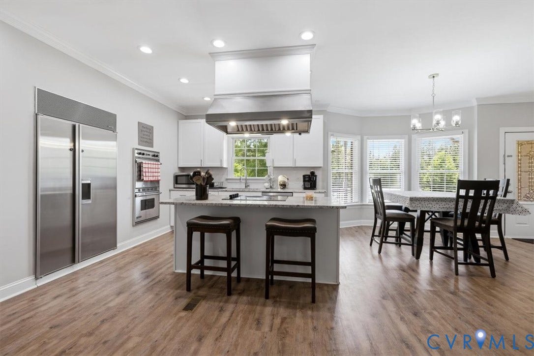 Spacious kitchen featuring wood-finish flooring, white cabinetry, and stainless steel appliances, including a built-in wall oven and a large refrigerator