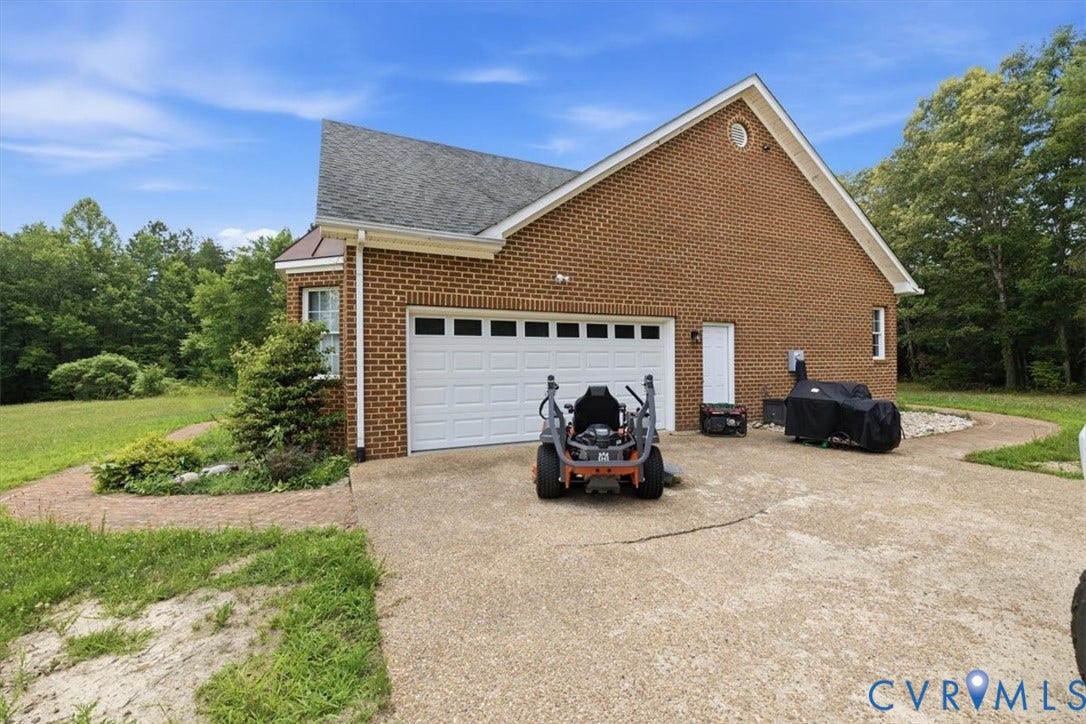 Brick exterior featuring a multi-car garage with a white panel door, a side entry door, and a gravel driveway