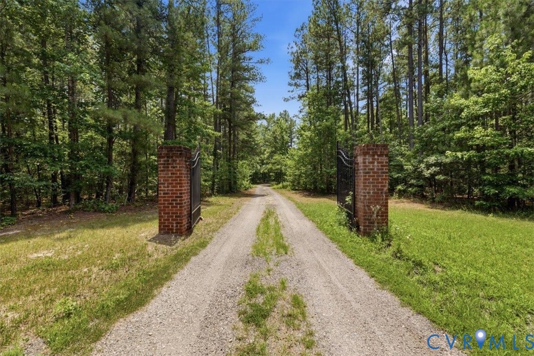 Gravel driveway flanked by mature trees and brick pillars with wrought iron gate sections