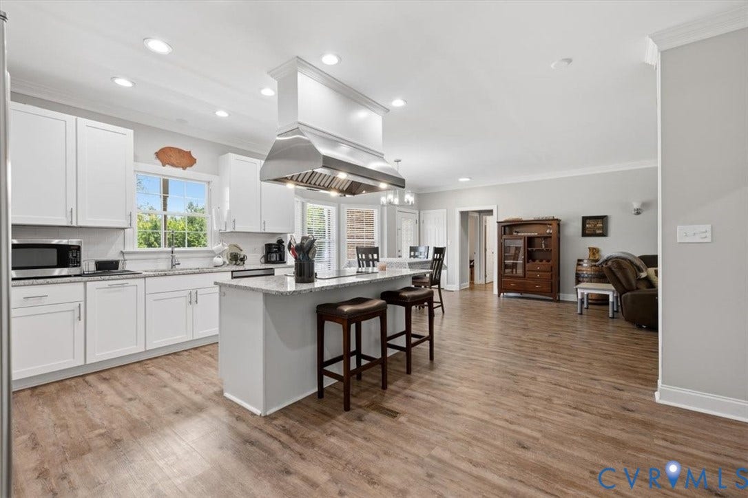 Open-concept kitchen featuring white shaker cabinetry, an island with seating, a stainless steel range hood, stone countertops, and wood-finish flooring
