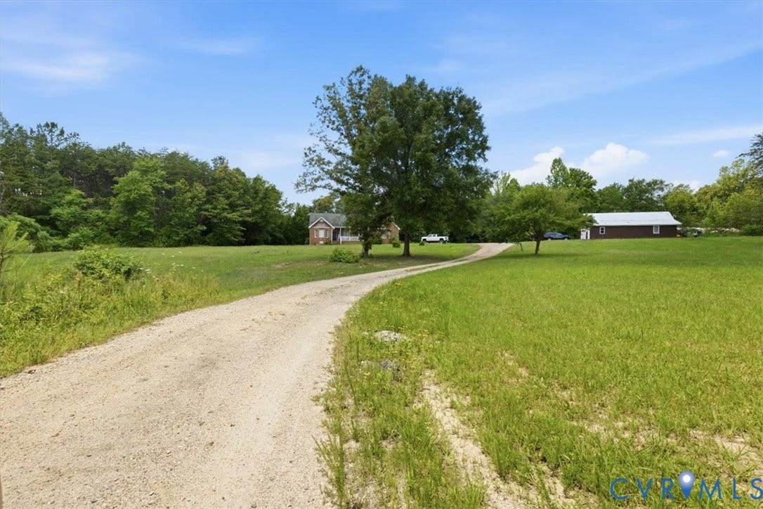 Curving gravel driveway leading to a brick residence with a white porch