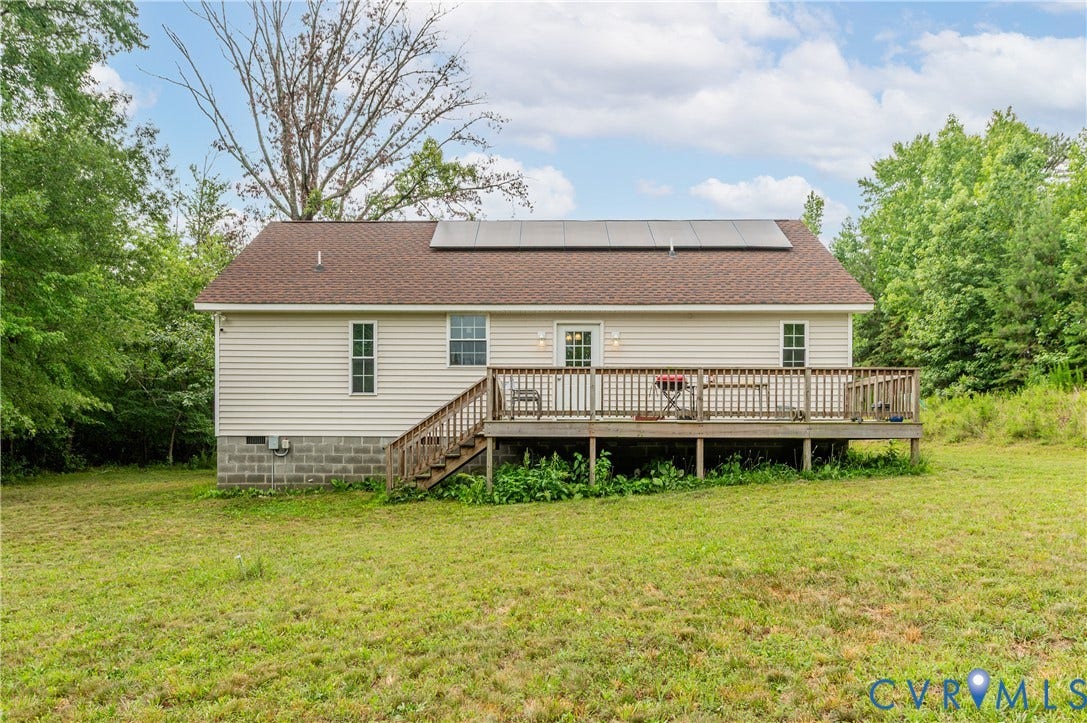 24580 St James Road, Amelia, VA 23083 Rear exterior featuring a spacious wood deck with steps, tan vinyl siding, a brown shingle roof, and visible solar panels
