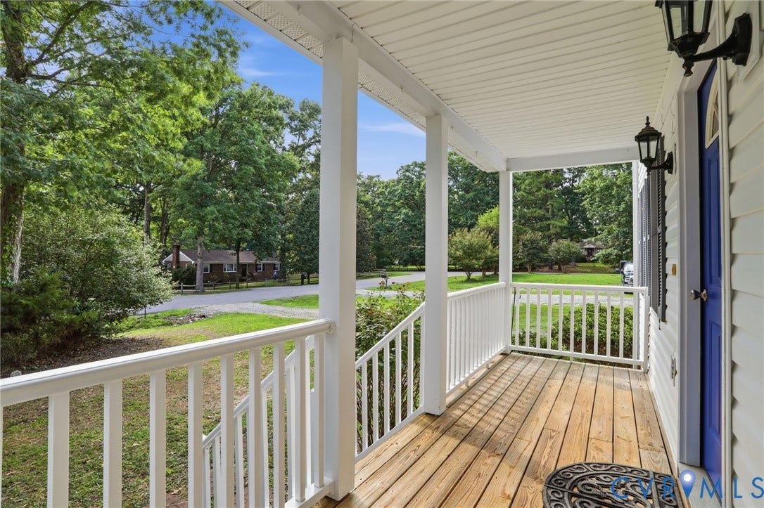 Inviting covered front porch with natural wood flooring, white railings, and a vibrant blue entry door